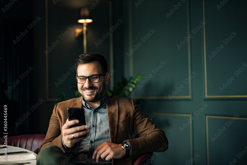 英俊微笑的男人在餐厅用智能手机发短信，肖像。