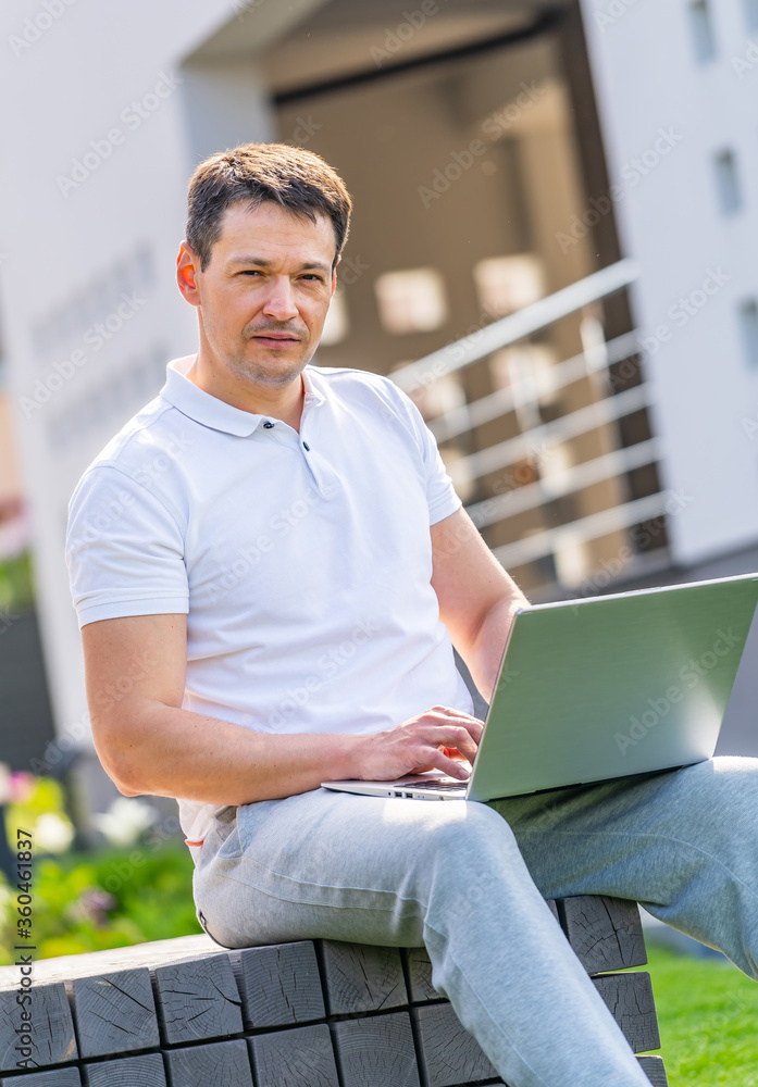 Handsome man working on his laptop outdoor. Sitting on bench.