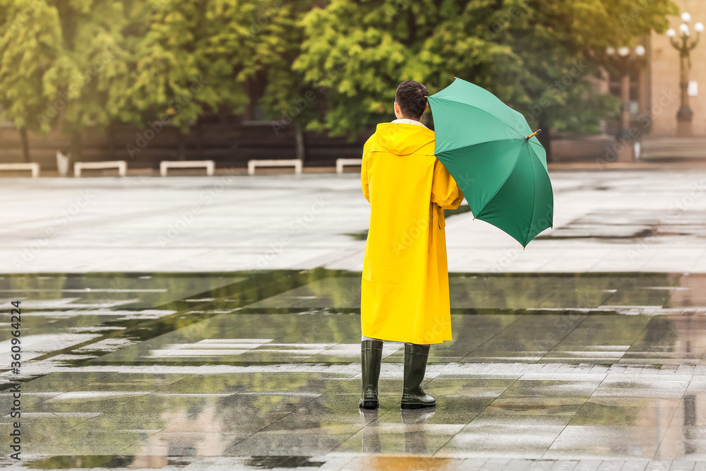 城市街道上一名身穿雨衣、打着雨伞的亚洲年轻男子