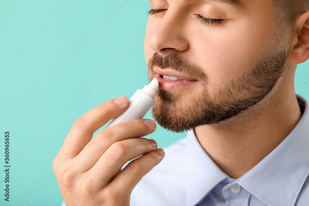 Handsome young man with lip balm on color background