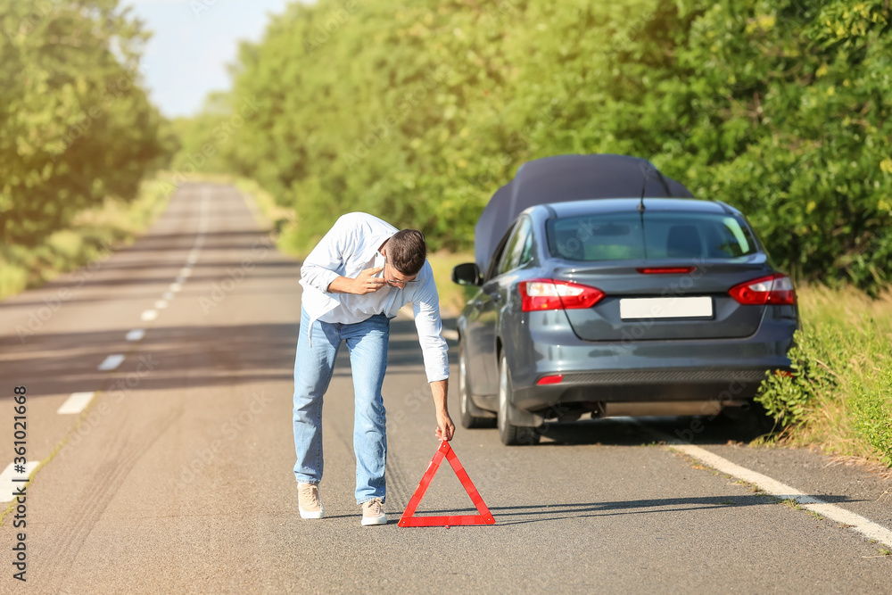 Young man with emergency stop sign near broken car on road