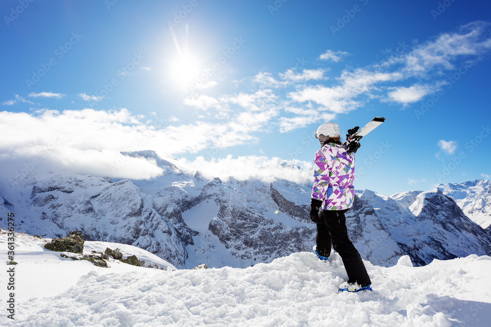 从后面看山地滑雪运动员站在山顶上，将滑雪板放在肩膀上向下看