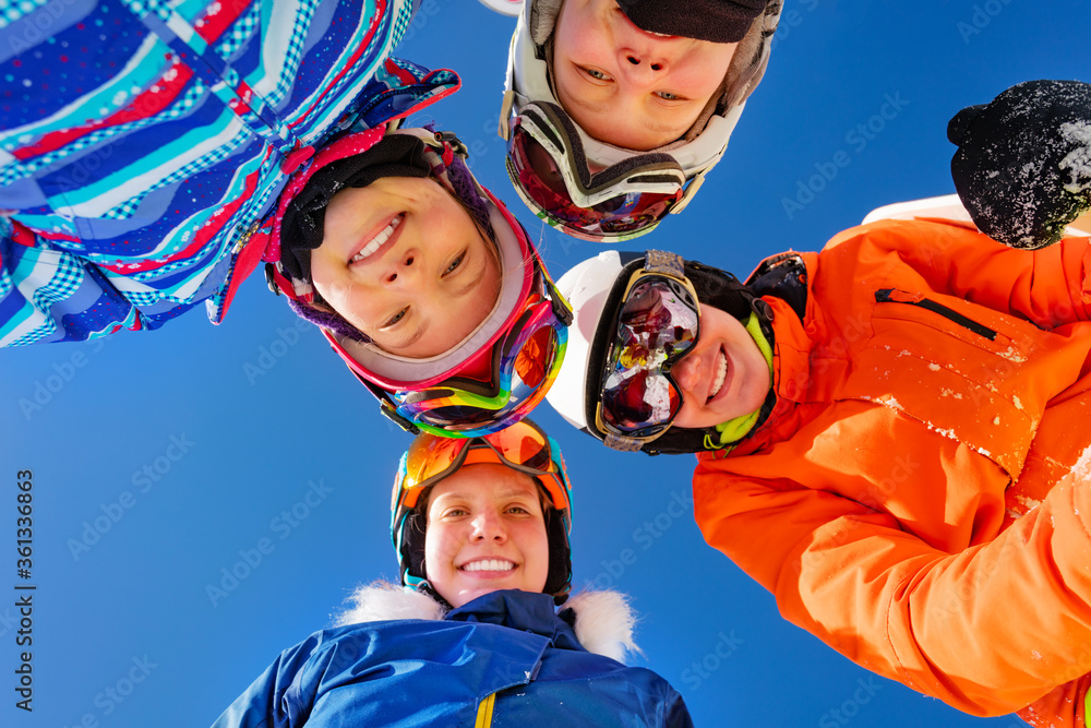 Group of children in ski outfit mask ang helmets look down standing together over blue sky