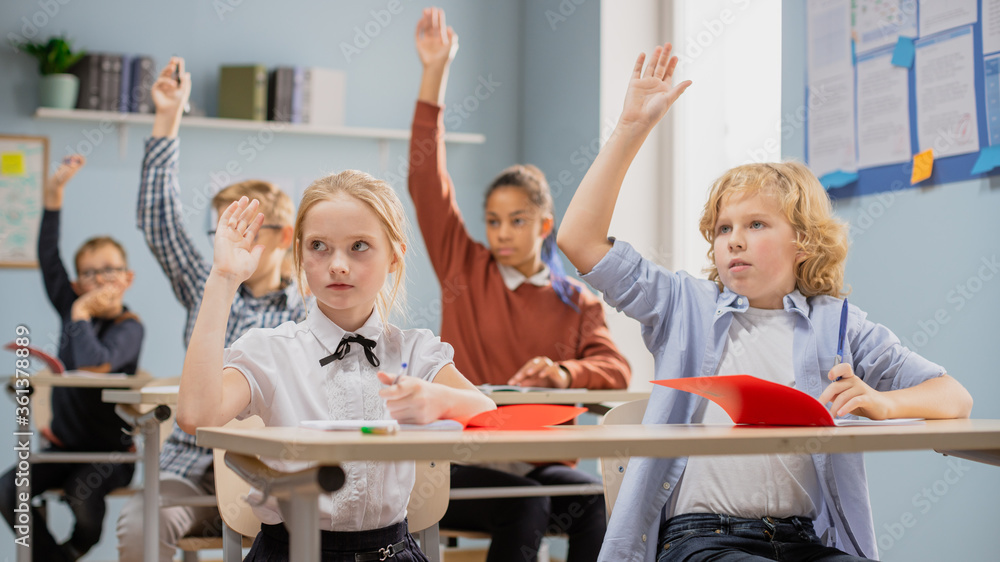 Elementary Classroom of Diverse Children Listening to the Teacher Giving a Lesson. Everyone Raises H