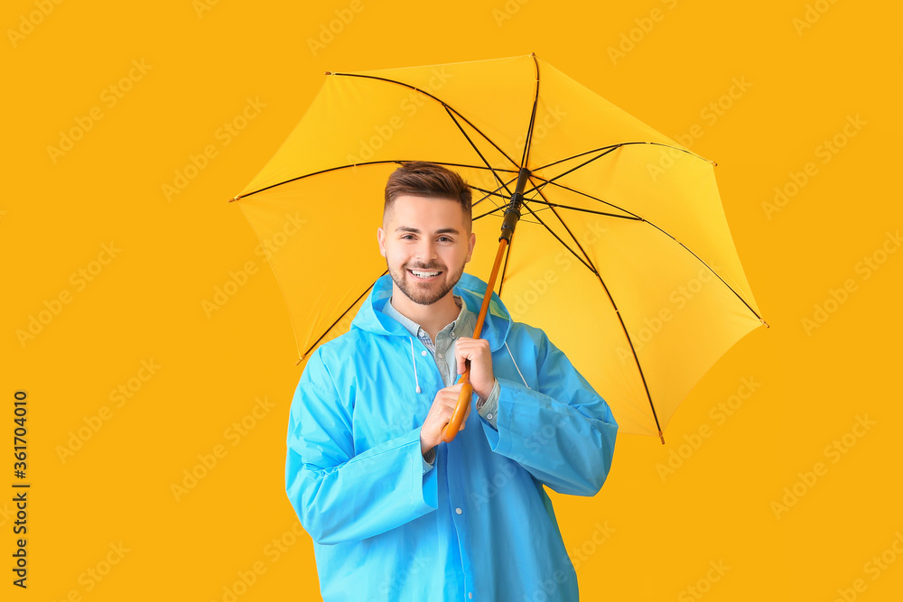 Young man in raincoat and with umbrella on color background