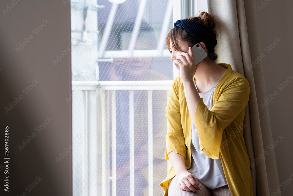 窓から外を眺めて電話をする女性