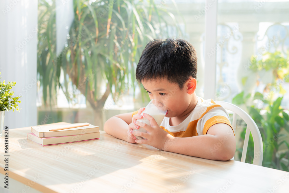 可爱的男孩做完作业后坐在桌子旁喝着一杯牛奶