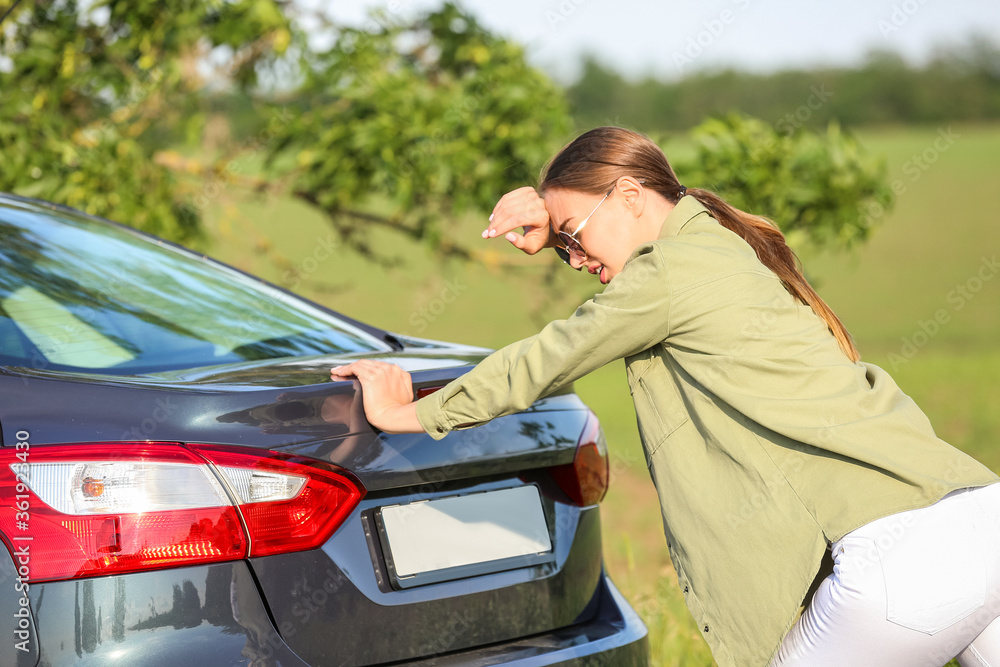 Young woman trying to push broken car on road