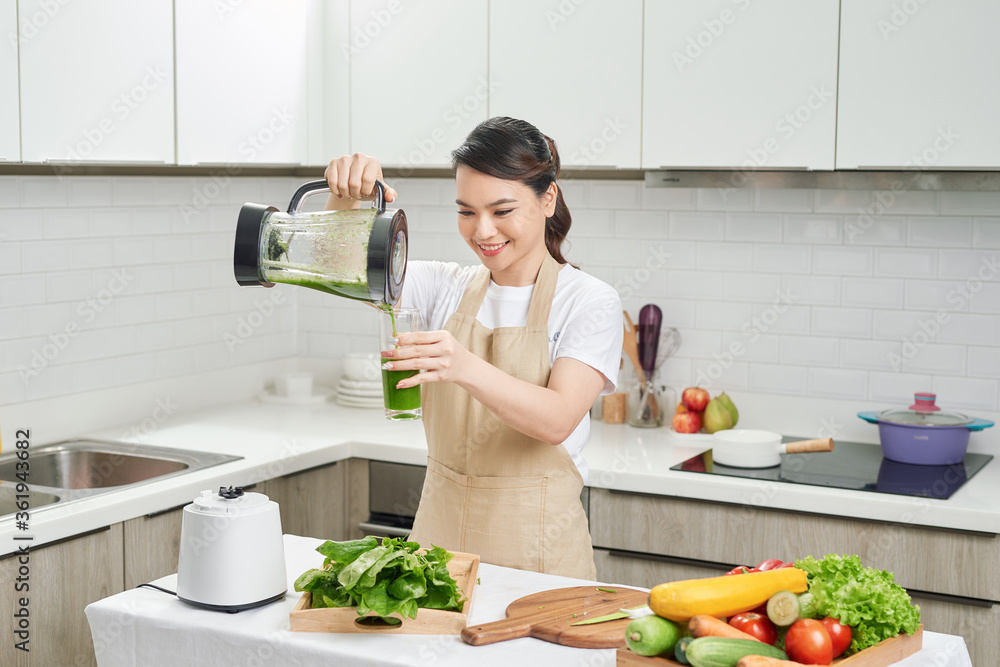 快乐的女人把她的新鲜鸡尾酒倒进白色厨房的玻璃杯里