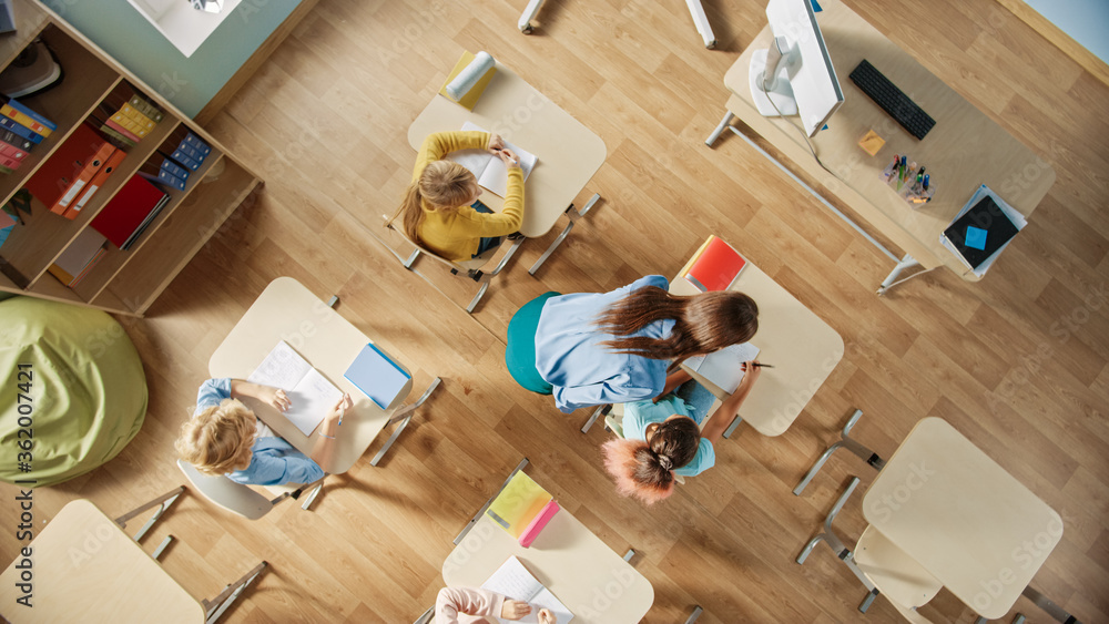 明亮的小学课堂：孩子们坐在学校的桌子旁工作，做作业，