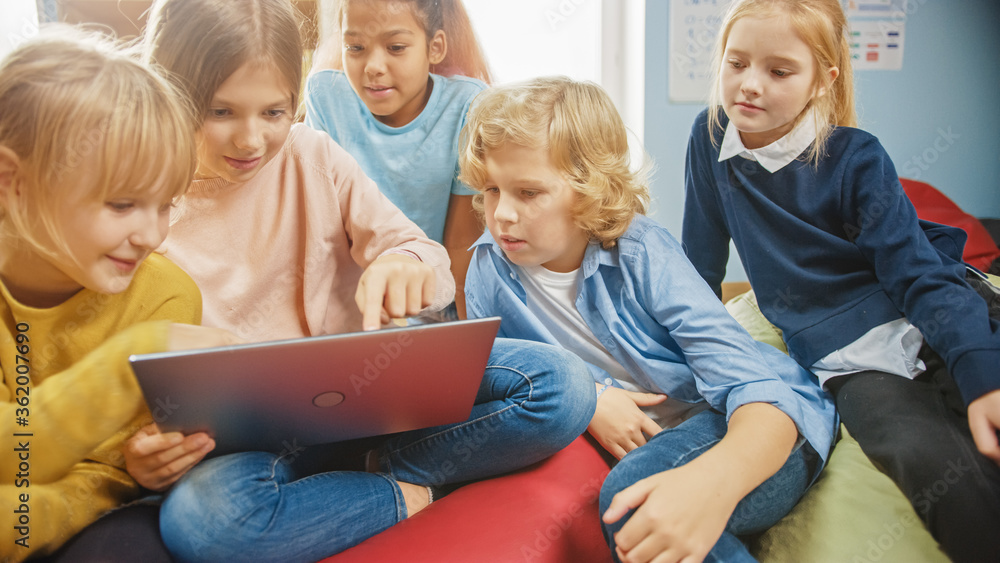 Diverse Group of Cute Small Children Sitting together on the Bean Bags Use Laptop Computer and Talk,