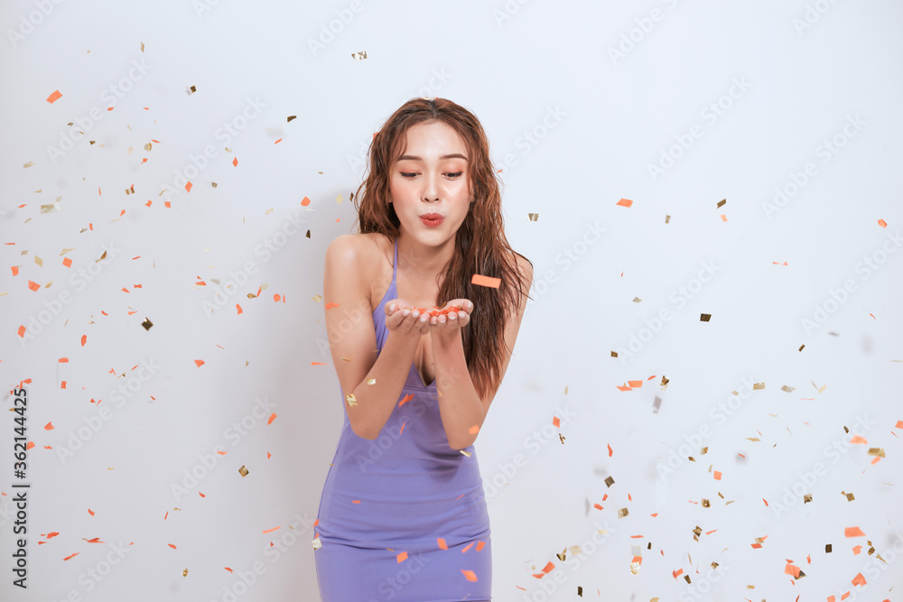 Beautiful young asian woman standing isolated over white background, standing under confetti