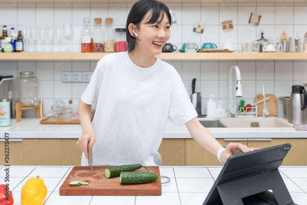 一个清纯的女孩一边切菜一边玩平板电脑