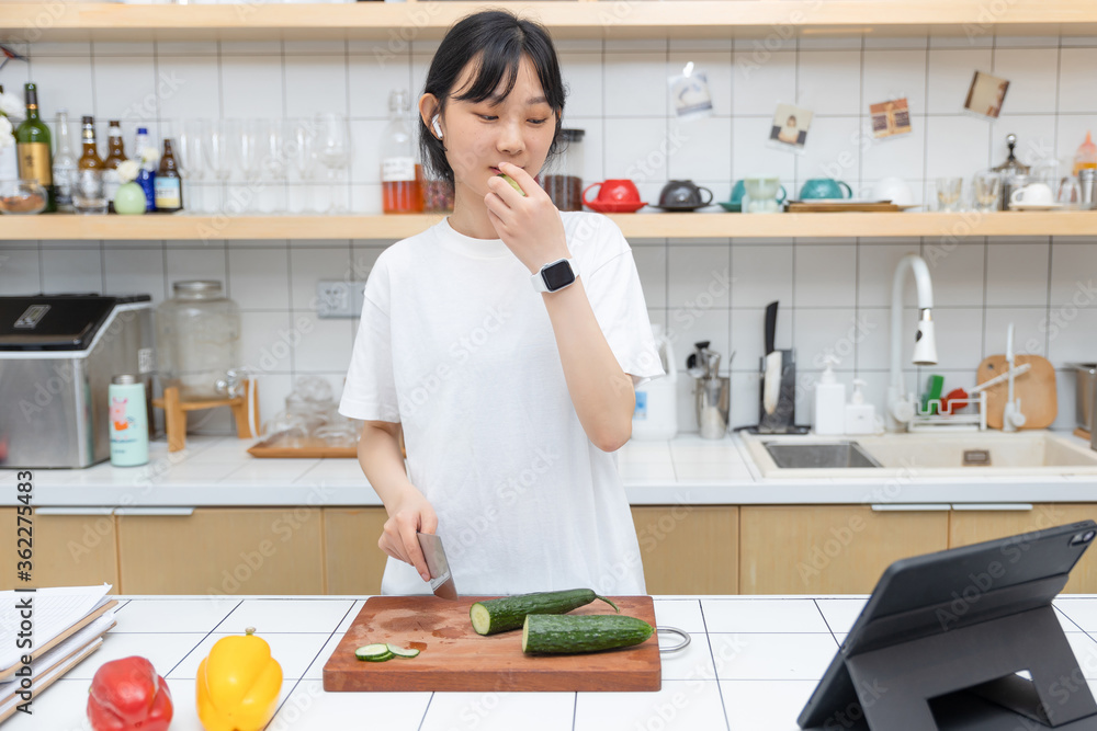 一个清纯的女孩一边切菜一边玩平板电脑