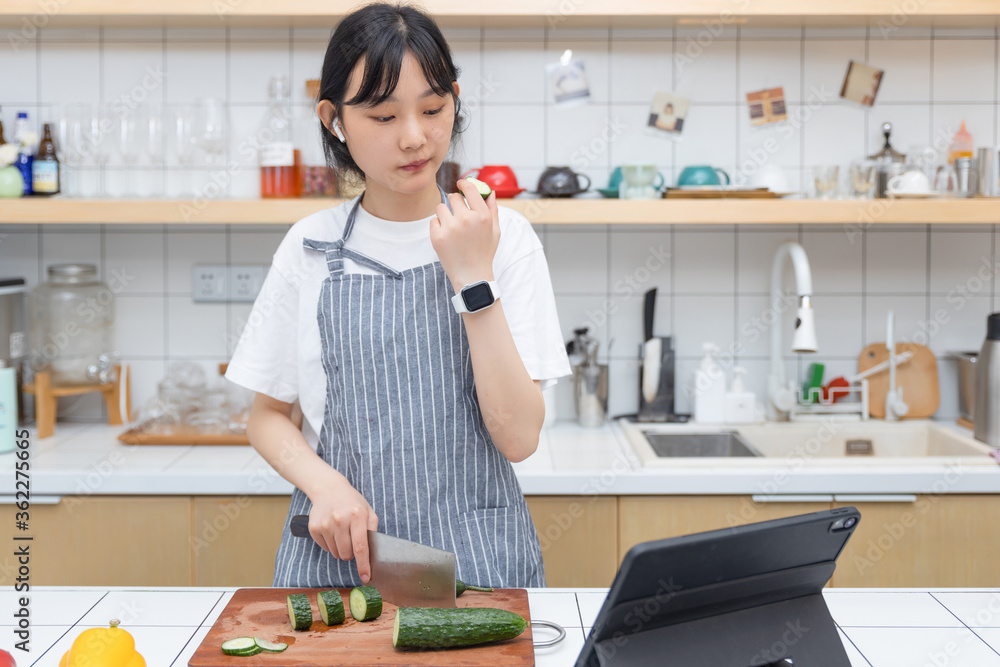 一个清纯的女孩一边切菜一边玩平板电脑