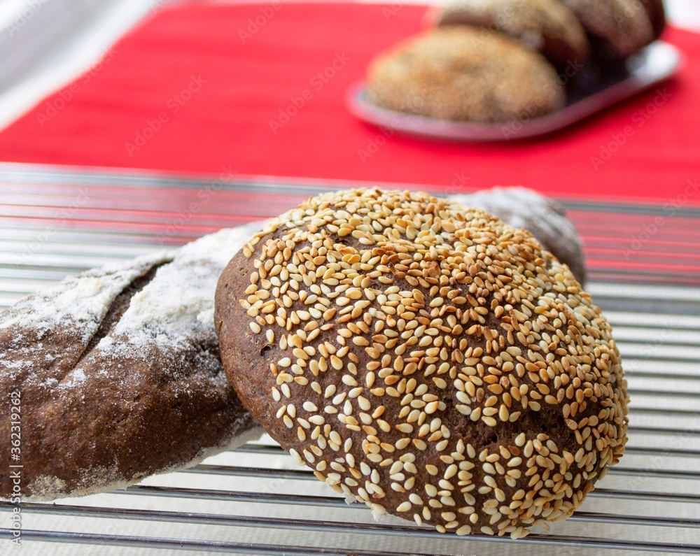 Composition in the bright rays of sunlight. Homemade rye bread (baguette and bun) on a metal wire ra