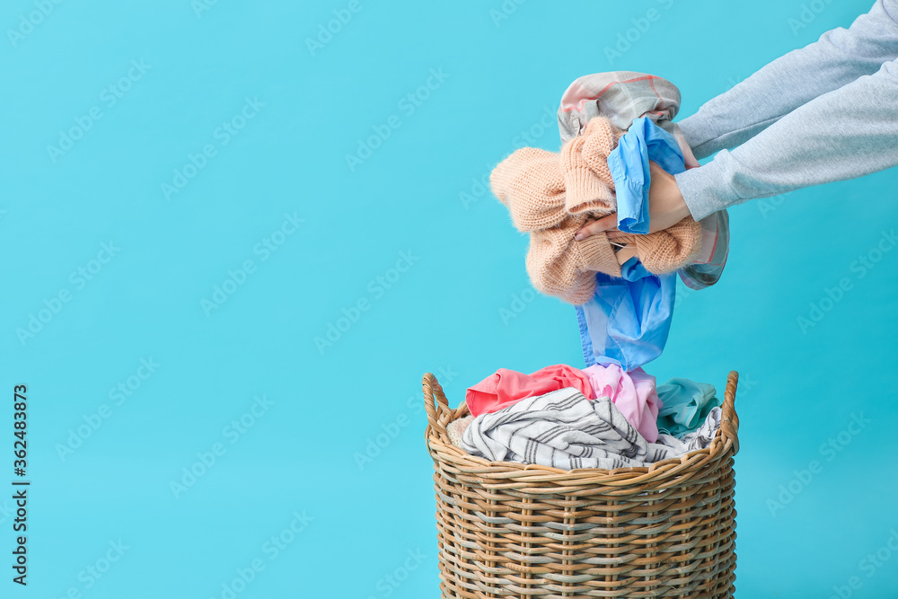 Woman putting dirty clothes in basket on color background