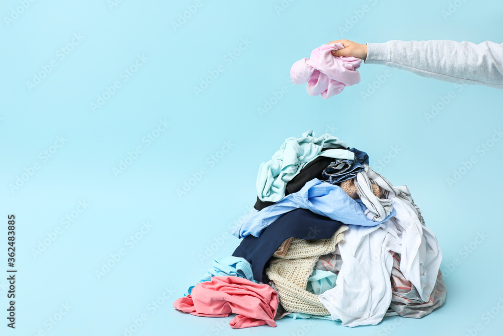 Female hand and heap of dirty clothes on color background