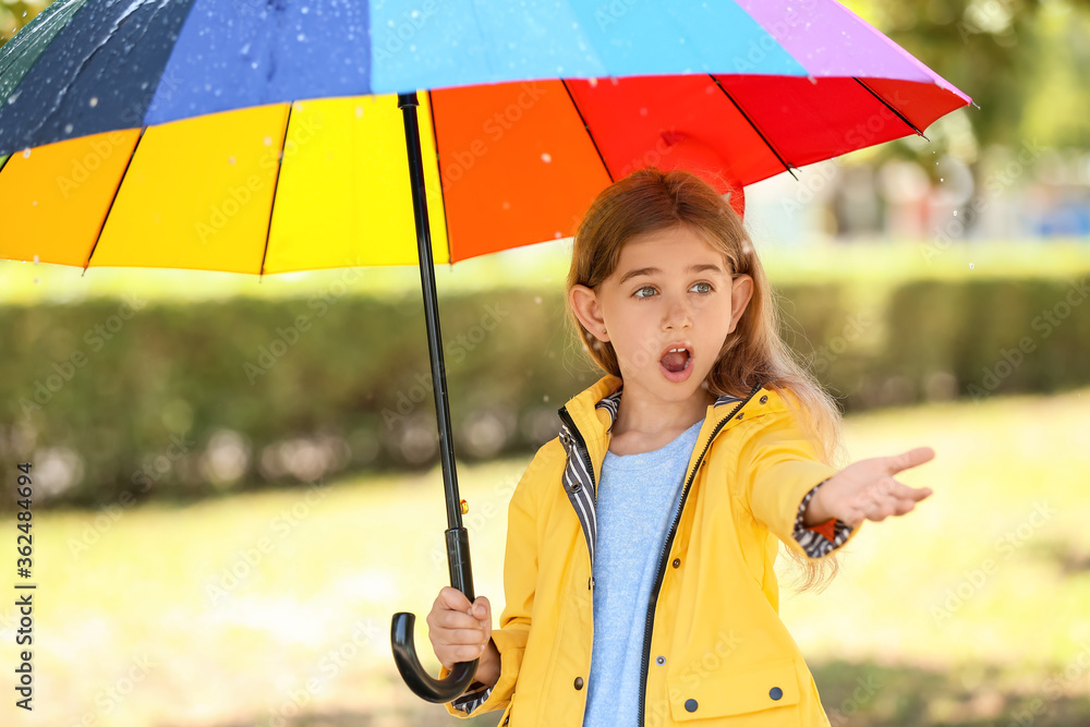 公园里带着雨伞、穿着雨衣的可爱小女孩