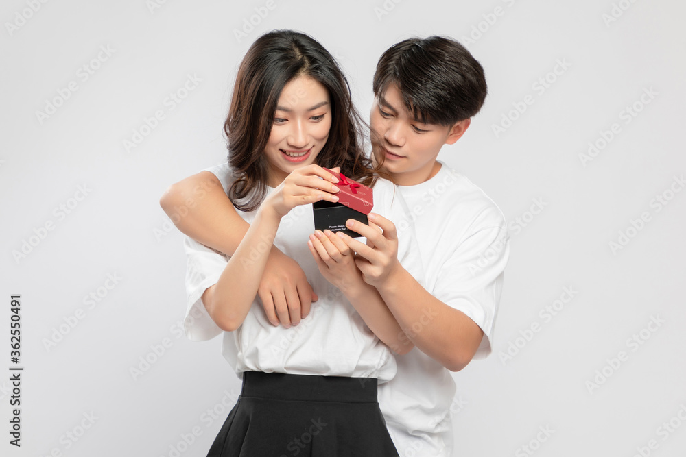 Young Asian lovers with gift boxes in their hands against a gray background

