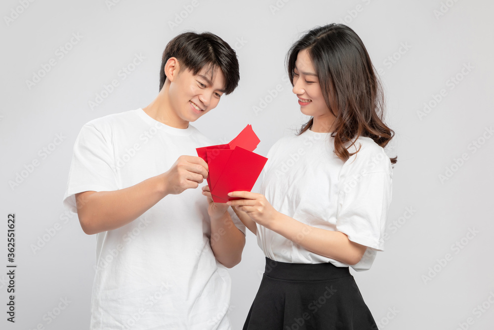 Young Asian lovers with red envelopes on New Years day in gray background

