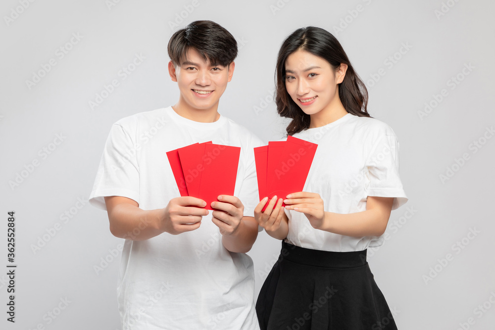 Young Asian lovers with red envelopes on New Years day in gray background

