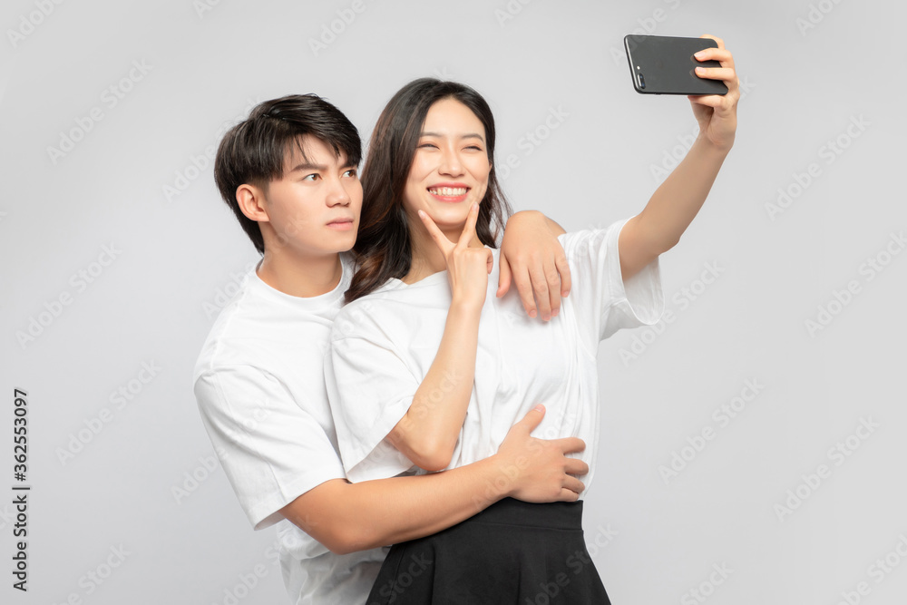 Young Asian lovers taking selfies against a gray background

