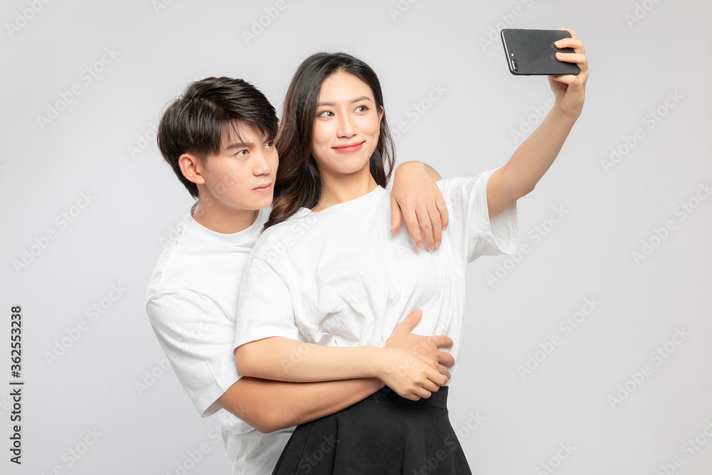 Young Asian lovers taking selfies against a gray background

