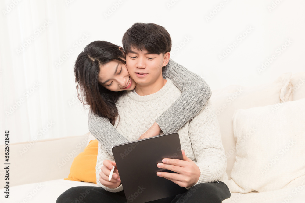 In winter, a young asian couple is sitting on a sofa using a tablet computer