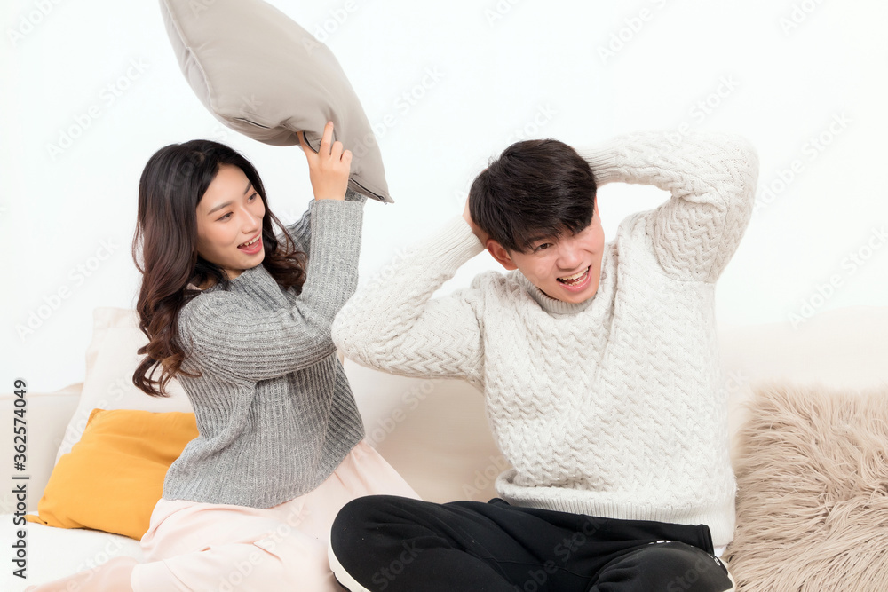 In winter, a pair of happy young Asian lovers are sitting on the sofa. The girl is beating the boy w