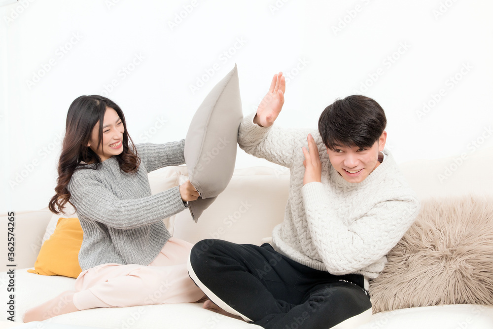 In winter, a pair of happy young Asian lovers are sitting on the sofa. The girl is beating the boy w