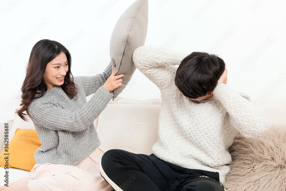 In winter, a pair of happy young Asian lovers are sitting on the sofa. The girl is beating the boy w