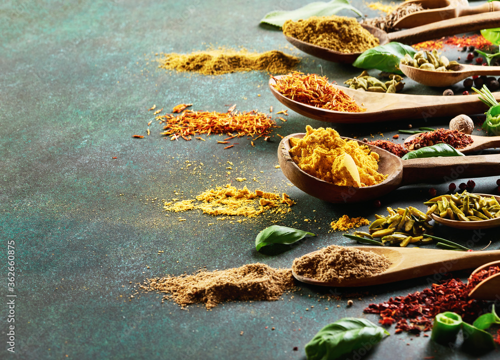 Various spice and dried herbs on dark green background.