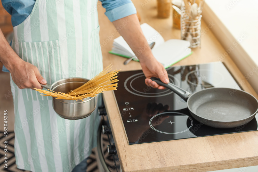 Young man boiling pasta in kitchen