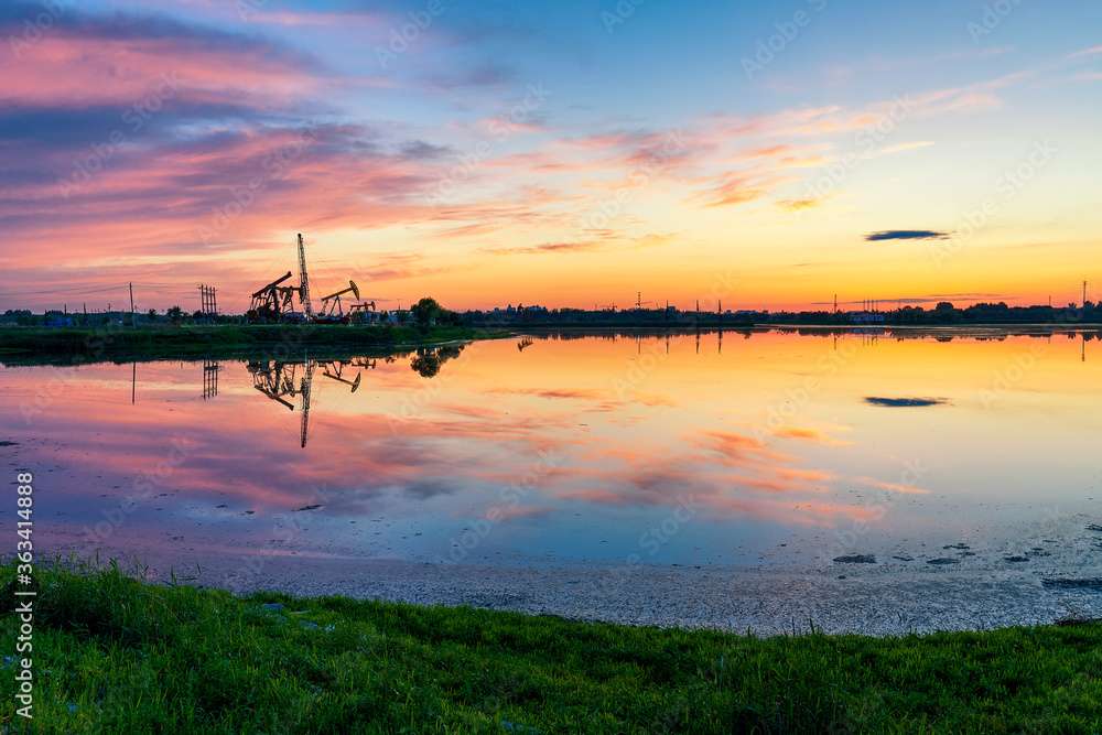 Oil Pumping Unit by the lake in the sunset.