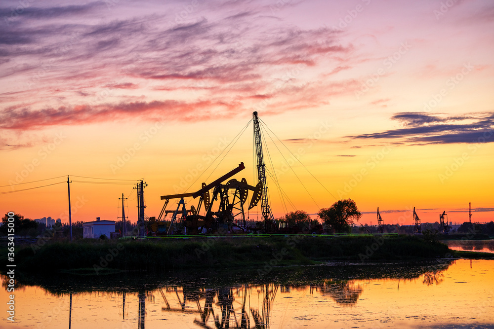 Oil Pumping Unit by the lake in the sunset.