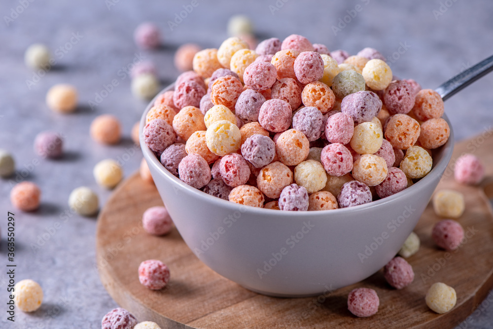 Colorful cereal corn balls mix, fruit flavor bowl sweets on gray cement background, close up, fresh,