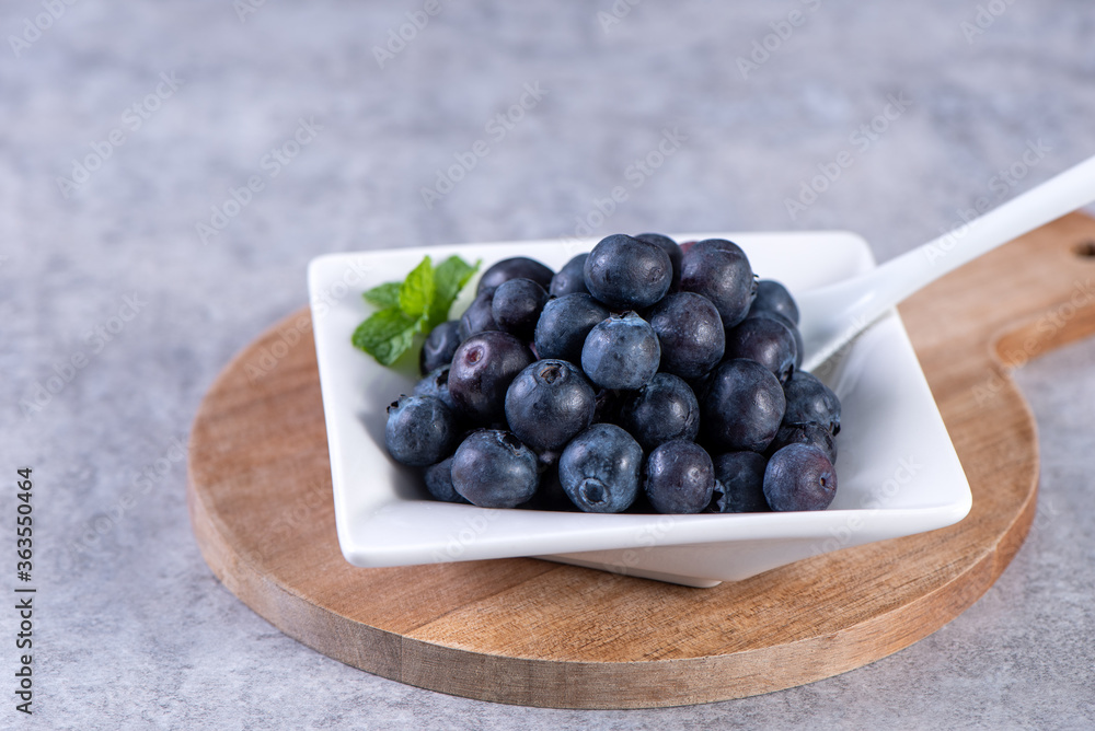 Pile of blueberry fruit in a bowl plate on a tray over gray cement concrete background, close up, he