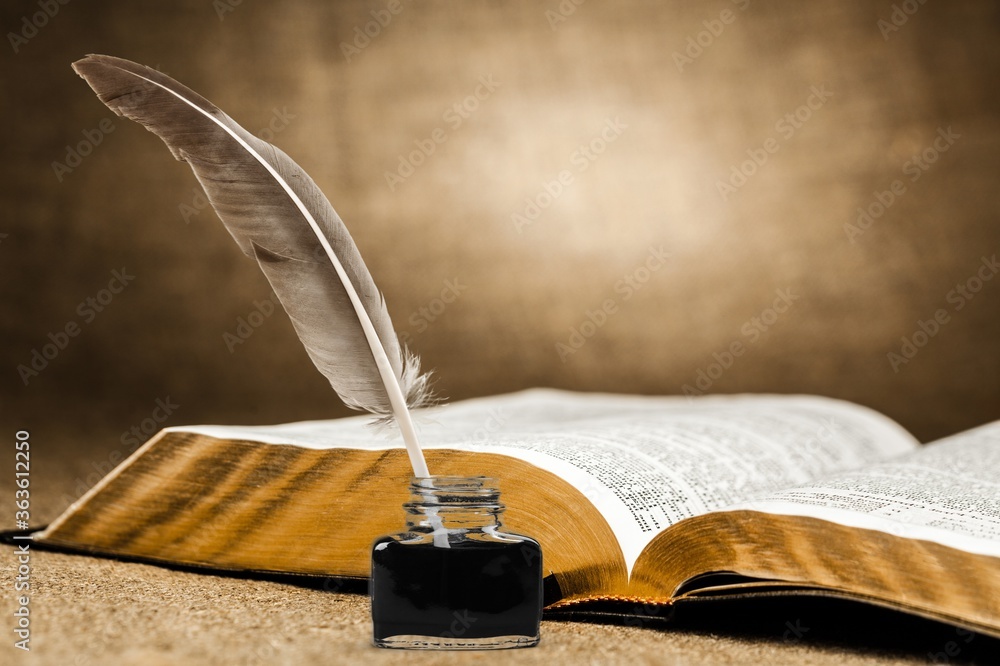 Feather quill pen and glass inkwell and open book