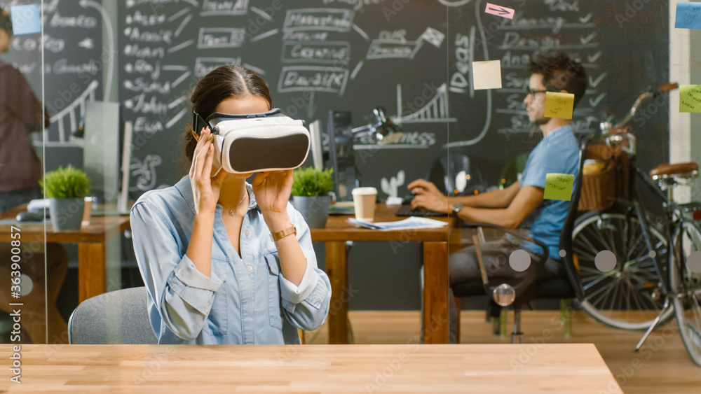 Young Female Creative Developer Wearing Virtual Reality Headset  Works on a Laptop, She Develops New