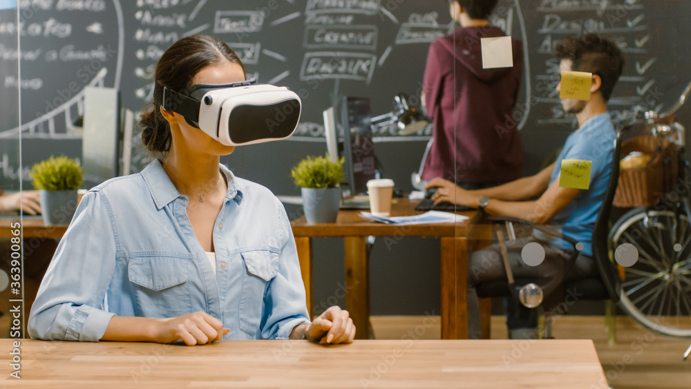 Young Female Creative Developer Wearing Virtual Reality Headset  Works on a Laptop, She Develops New