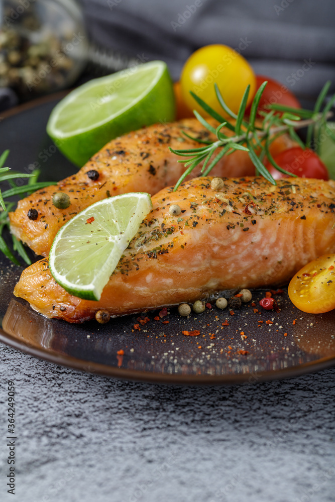 Two grilled filet salmon steaks with herbs, tomatoes, lime and spices on a ceramic plate.