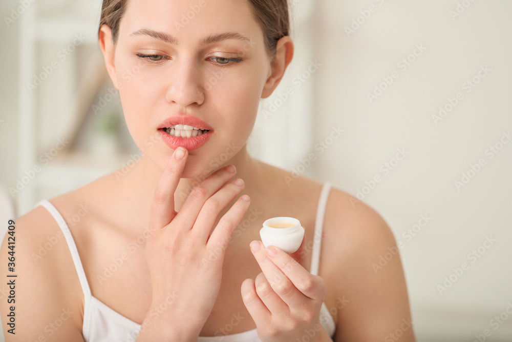 Beautiful young woman with lip balm at home