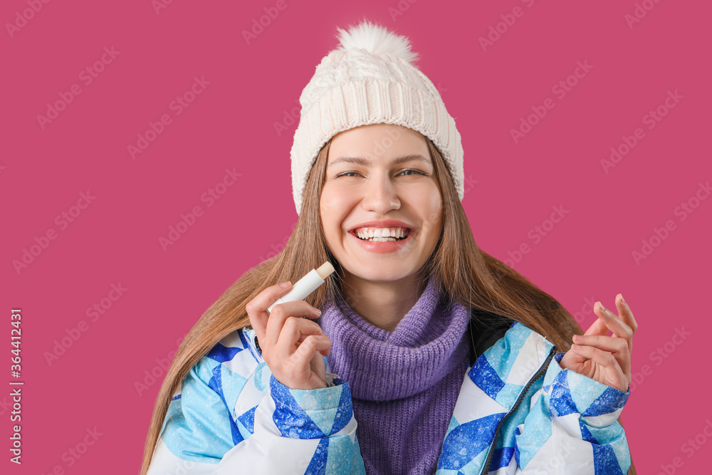 Beautiful young woman with lip balm on color background