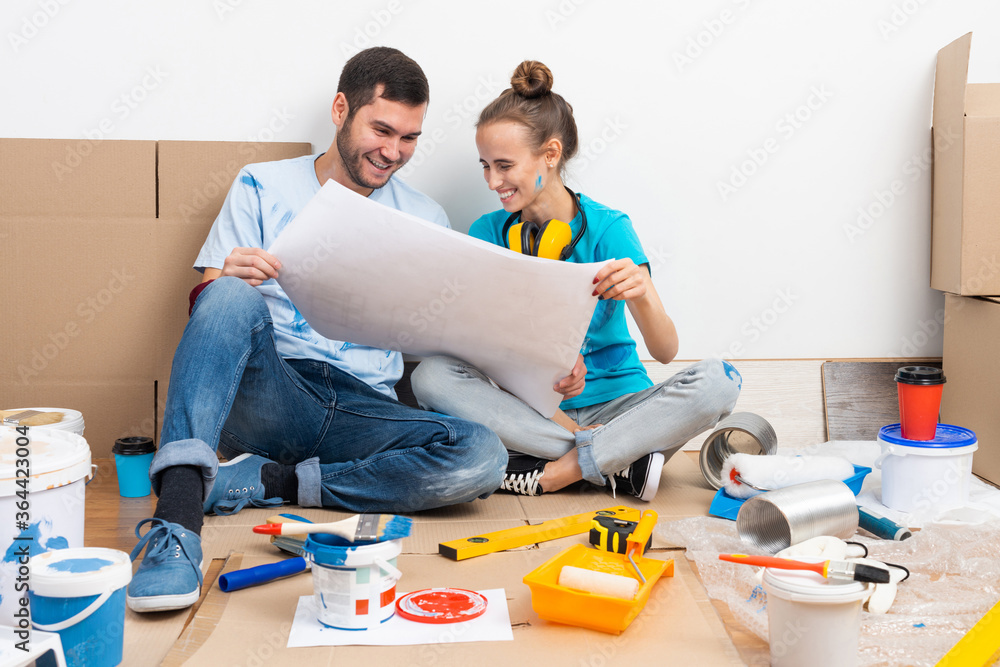 Happy couple sitting on floor with blueprint.