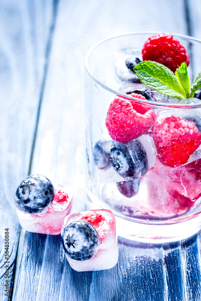 glass with frozen berries in cubes on wooden desk background