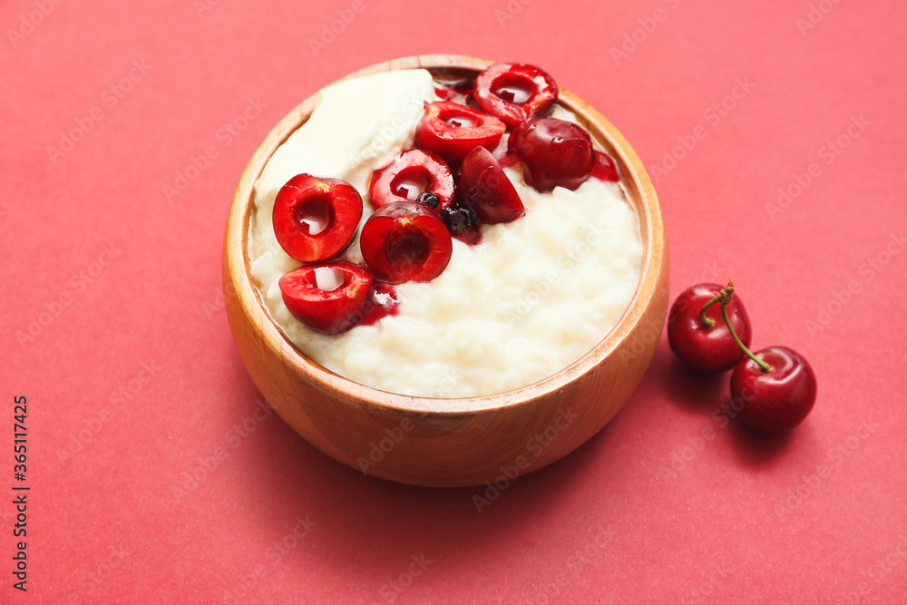 Bowl with boiled rice and cherry on color background