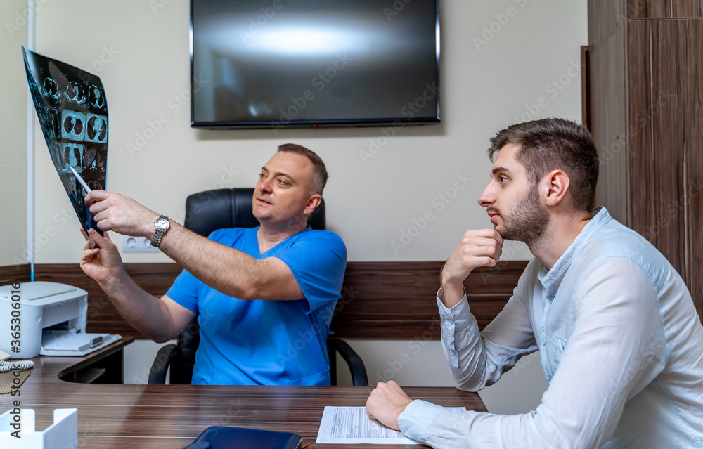 Doctor explaining an x-ray image to patient in medical office. Male patient at doctor`s office.