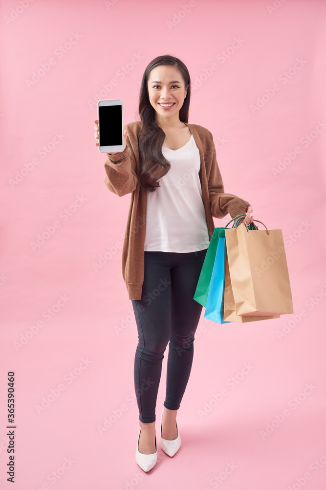 Photo of pretty woman holding shopping bags, showing blank mobile screen, over pink background