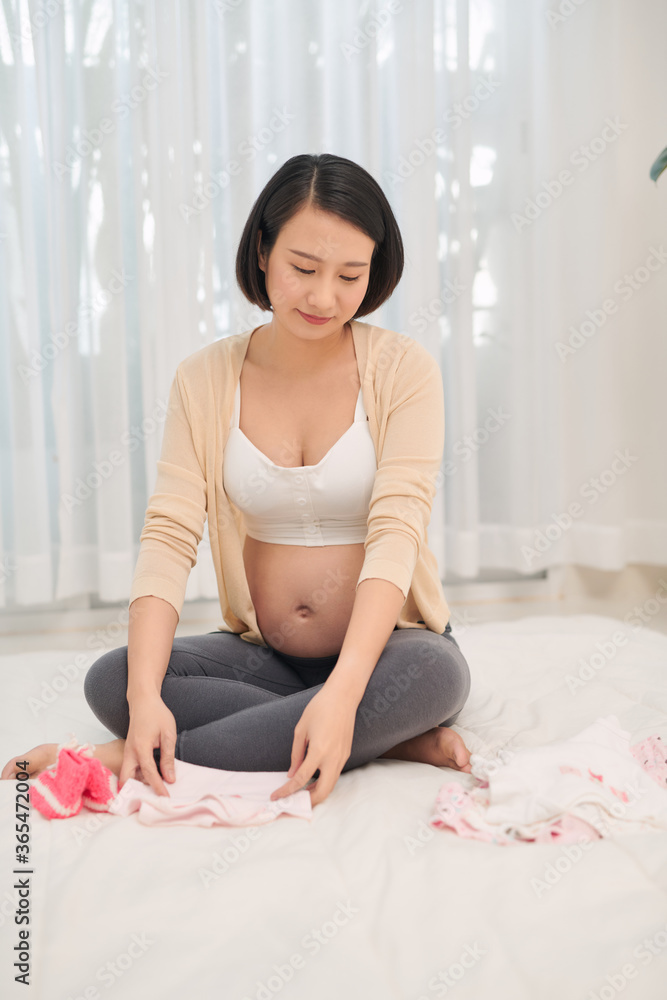 Happy future mother holding in hands cute bodywear for newborn. Concept of parenthood, preparing dur